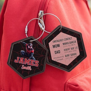May include: Two hexagonal bag tags with a black spiderweb pattern. One tag features a Spider-Man graphic, the name JAMES SMITH in red, and a metal ring. The other tag displays EMERGENCY CONTACT information for MOM, DAD, and an Alternative Contact.
