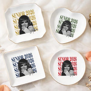 May include: Four white ceramic trinket dishes in various shapes: square, heart, round, and a scalloped edge. Each dish features a black and white image of a person wearing sunglasses, with the text "SENIOR 2026" in different colours. Gold trim.