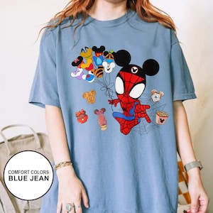 Puede incluir: Camiseta azul vaquero con un personaje de dibujos animados de Spider-Man con orejas de Mickey Mouse. El dise&ntilde;o incluye globos con tem&aacute;tica de Mickey Mouse y varios alimentos. La camiseta tiene el texto "COMFORT COLORS BLUE JEAN" en un c&iacute;rculo blanco.