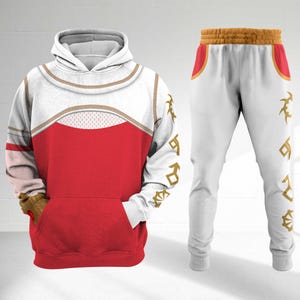 May include: A white and red hoodie and matching sweatpants set. The hoodie has a white hood and sleeves with gold trim and a red body. The sweatpants are white with gold accents and designs. The set is a matching outfit.
