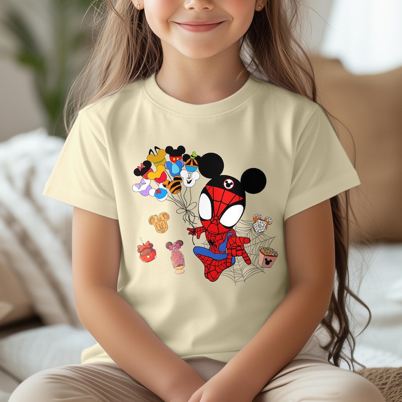 Puede incluir: Camiseta beige claro con una ilustraci&oacute;n de dibujos animados de Spider-Man con orejas de Mickey Mouse sosteniendo globos. Los globos est&aacute;n dise&ntilde;ados como varios personajes de Disney. Tambi&eacute;n se incluyen golosinas tem&aacute;ticas de Disney y una telara&ntilde;a.