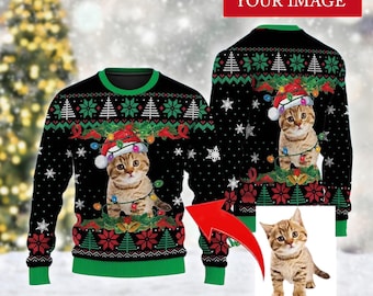 May include: Black Christmas sweater featuring a tabby cat wearing a Santa hat and string lights. The sweater has green and red accents, snowflakes, and Christmas tree patterns. The text "CUSTOM YOUR IMAGE" is at the top.