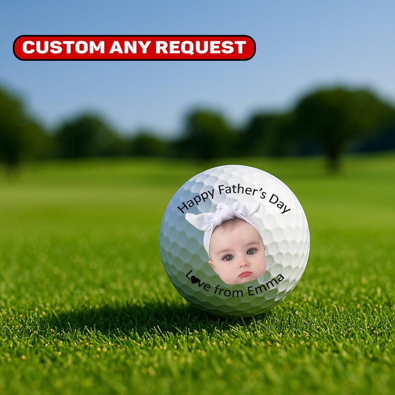May include: A personalized golf ball with a baby's face and the text "Happy Father's Day, Love from Emma." The golf ball is white and sits on green grass. The top of the image has a red banner with the text "CUSTOM ANY REQUEST."