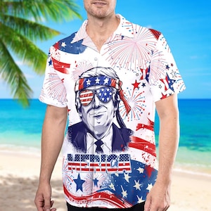 May include: A white short-sleeved button-up shirt with a cartoon image of a person wearing sunglasses and a bandana with stars and stripes. The shirt has a red, white and blue American flag pattern with fireworks and stars. The word "MERICA" is printed on the shirt.