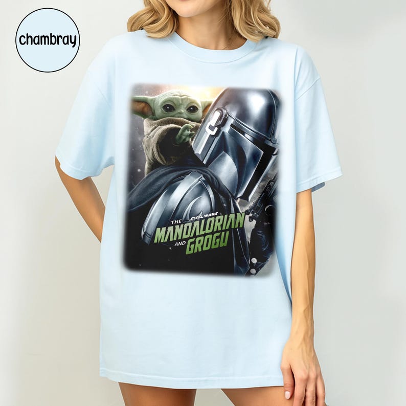 May include: Light blue t-shirt featuring a graphic of The Mandalorian and Grogu from Star Wars. The design includes the Mandalorian's helmet and Grogu, with the text "The Star Wars Mandalorian and Grogu".