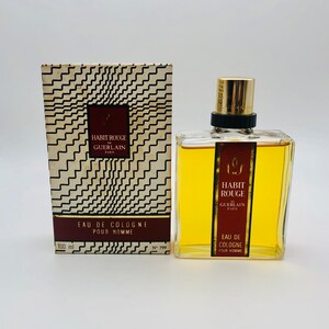 May include: A 100 ml bottle of cologne in a clear glass bottle with a gold cap. The bottle is labeled "Habit Rouge" by Guerlain Paris. The bottle is sitting on a white surface.