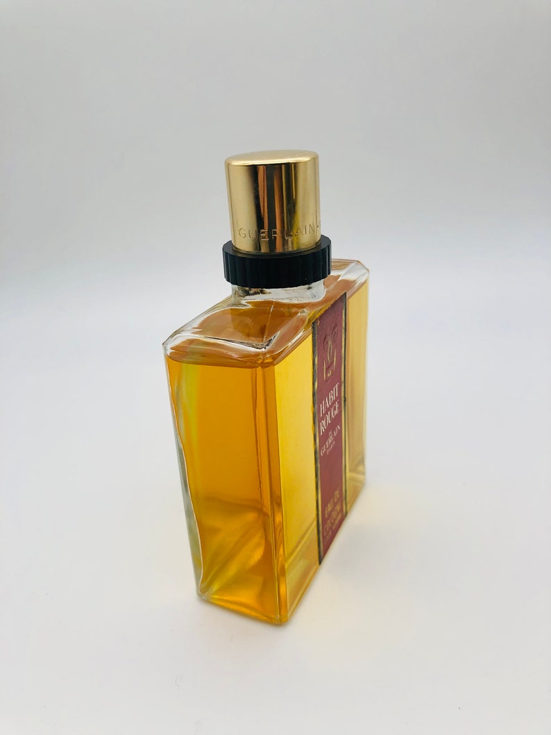 May include: A clear glass bottle of Guerlain Habit Rouge perfume with a gold cap and a red label. The label reads "Habit Rouge Guerlain Eau de Cologne".