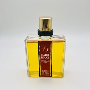 May include: A clear glass bottle of cologne with a gold cap and label. The label reads "Habit Rouge de Guerlain Paris Eau de Cologne Pour Homme".