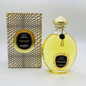 Könnte beinhalten: Eine Vintage-Flasche Chamade Eau de Toilette von Guerlain. Die Flasche ist aus klarem Glas mit einem goldenen Verschluss und einem goldenen Etikett. Das Etikett trägt die Aufschrift "eau de toilette chamade guerlain paris". Die Flasche steht auf einer weißen Oberfläche.
