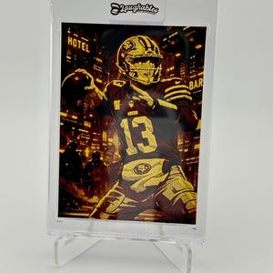 May include: A gold-toned football card featuring a player in a maroon and gold uniform, throwing a football. The background shows a cityscape. The card is in a protective case, with the "Laughables" logo at the top.