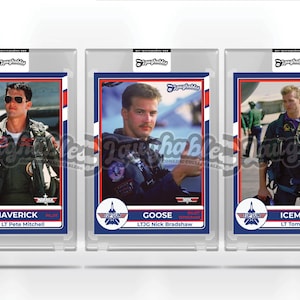 May include: Three trading cards featuring characters from the movie Top Gun. The cards are in protective plastic cases. The cards feature Maverick, Goose, and Iceman. Each card has a blue, red, and white color scheme with a picture of the character and their name and rank.