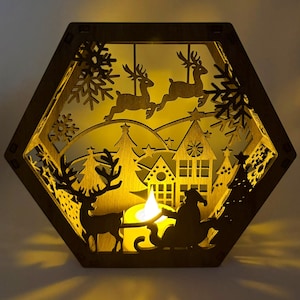 May include: A wooden, hexagonal Christmas lantern with a festive scene. The lantern features cut-out silhouettes of reindeer, houses, trees, snowflakes, and Santa in his sleigh. A warm, yellow light shines from within, creating a cozy holiday ambiance.