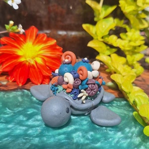 May include: A grey turtle figurine with a colourful coral reef design on its back. The turtle is sitting on a blue and green surface.