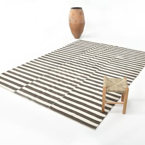 May include: A black and white striped rug with a small wooden stool with a woven seat.
