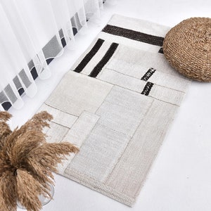 Peut inclure: Un tapis rayé blanc et noir avec un coussin rond tissé sur une surface blanche. Le tapis est fait de différents morceaux de tissu cousus ensemble.