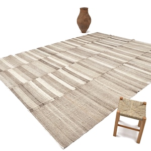 Pode incluir: Um tapete grande, retangular, tecido à mão com um padrão listrado em tons de bege e branco. O tapete é feito de fibras naturais e tem um visual rústico e orgânico.