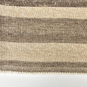 May include: Close-up of a brown and beige striped woven rug with a fringed edge.
