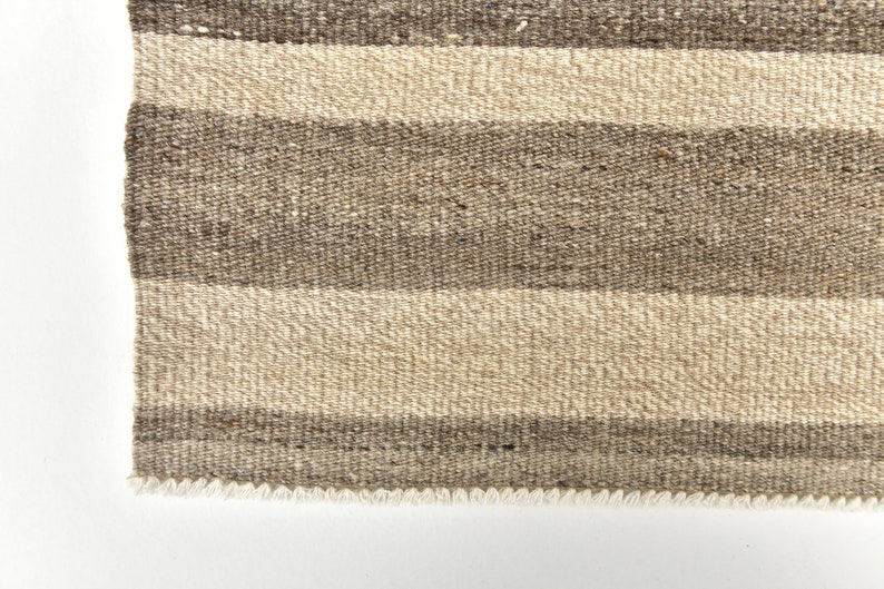 May include: Close-up of a brown and beige striped woven rug with a fringed edge.