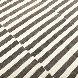 May include: A white and brown striped rug with a woven texture. The rug is made of natural fibers and has a simple, modern design.