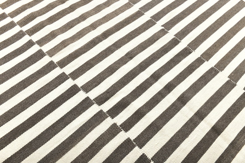 May include: A white and brown striped rug with a woven texture. The rug is made of natural fibers and has a simple, modern design.