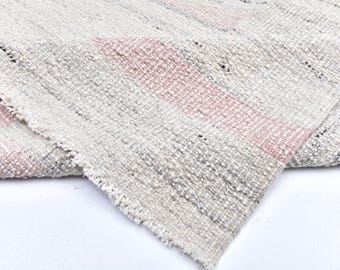 May include: Close-up of a woven textile with a light gray and pink striped pattern. The fabric has a textured appearance with visible threads and a frayed edge. The textile is folded over, revealing its layered construction.