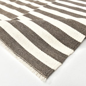 May include: Close-up of a brown and white striped rug with a fringe edge. The rug is made of a woven material and has a natural, rustic look.