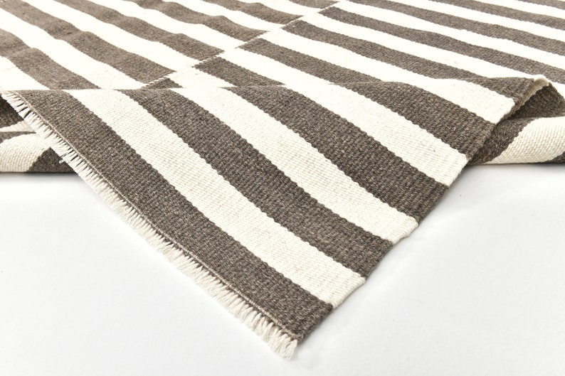 May include: Close-up of a brown and white striped rug with a fringe edge. The rug is made of a woven material and has a natural, rustic look.