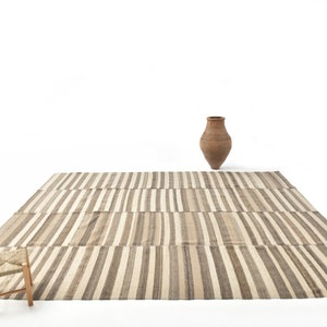 May include: A striped rug with a woven stool and a terracotta vase on a white background.
