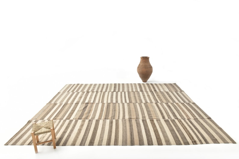 May include: A striped rug with a woven stool and a terracotta vase on a white background.