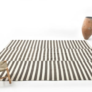 May include: A black and white striped rug with a woven stool in the foreground. A terracotta vase is in the background.