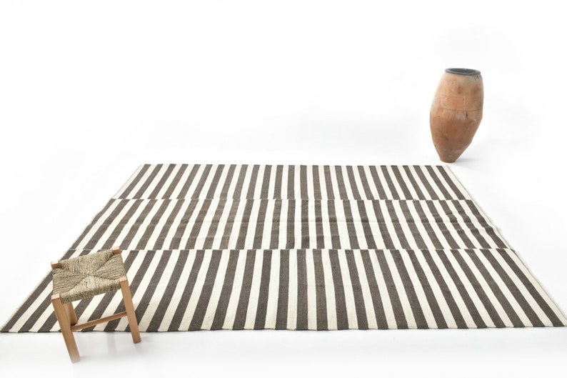 May include: A black and white striped rug with a woven stool in the foreground. A terracotta vase is in the background.