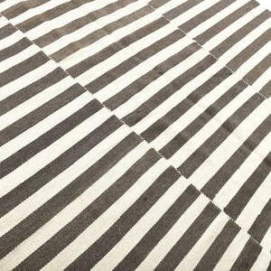 May include: A white and brown striped rug with a geometric pattern. The rug is made of a woven material and has a soft texture.