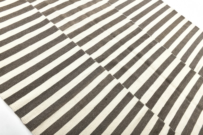 May include: A white and brown striped rug with a geometric pattern. The rug is made of a woven material and has a soft texture.