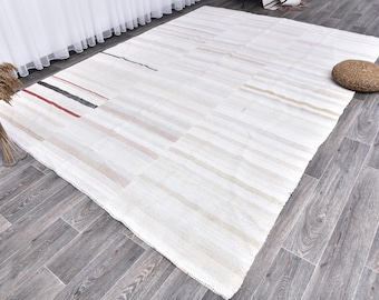 Può includere: Tappeto bianco tessuto con un motivo a strisce in nero, rosso e grigio. Il tappeto è steso su un pavimento in legno grigio.