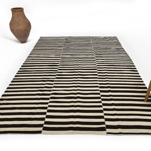 May include: Black and white striped rug with a subtle gradient effect. The rug is made of wool and has a hand-woven texture.