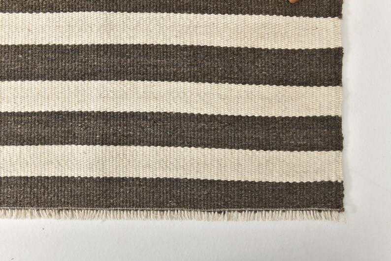 May include: A brown and white striped rug with a fringe border. The rug is made of a woven material and has a subtle texture.