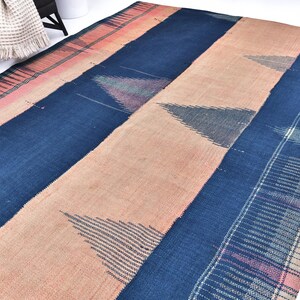 May include: A large, rectangular rug with a striped design. The rug features alternating bands of navy blue, peach, and light beige. Geometric triangle patterns are visible within the peach sections. The rug is made of woven fabric.