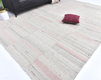 May include: A rectangular rug with a light gray and pink striped pattern. The rug has a textured appearance and is made of woven material. A maroon pillow rests on the rug.
