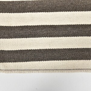 May include: A white and brown striped rug with a fringed edge.