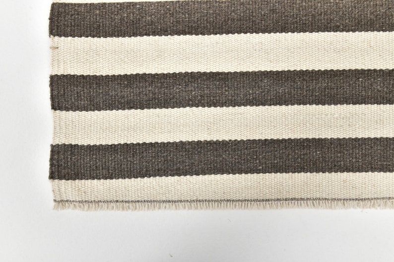 May include: A white and brown striped rug with a fringed edge.