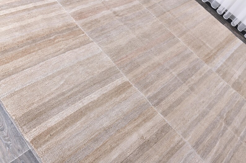 Pu&ograve; includere: Un tappeto a strisce beige e bianco con una trama tessuta. Il tappeto ha una lucentezza discreta e un design contemporaneo.