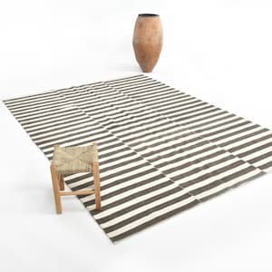 May include: A black and white striped rug with a wooden stool with a woven straw seat. The rug is on a white background.