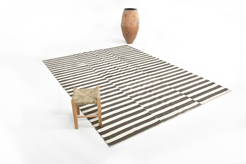 May include: A black and white striped rug with a wooden stool with a woven straw seat. The rug is on a white background.