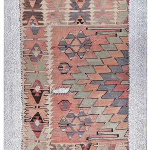 May include: Rectangular rug with a geometric pattern in shades of peach, gray, and green. The rug features diamond and zigzag designs, with a white border. The rug measures 4.7 feet by 3.4 feet.