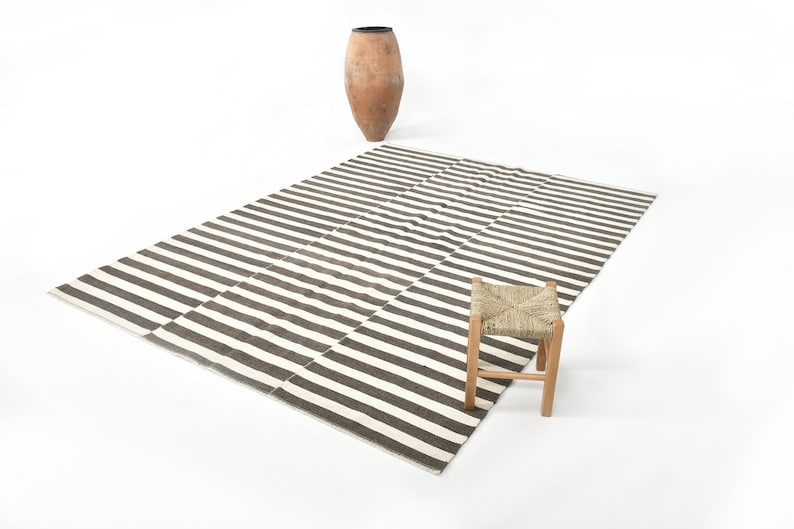 May include: A black and white striped rug with a small wooden stool with a woven seat.