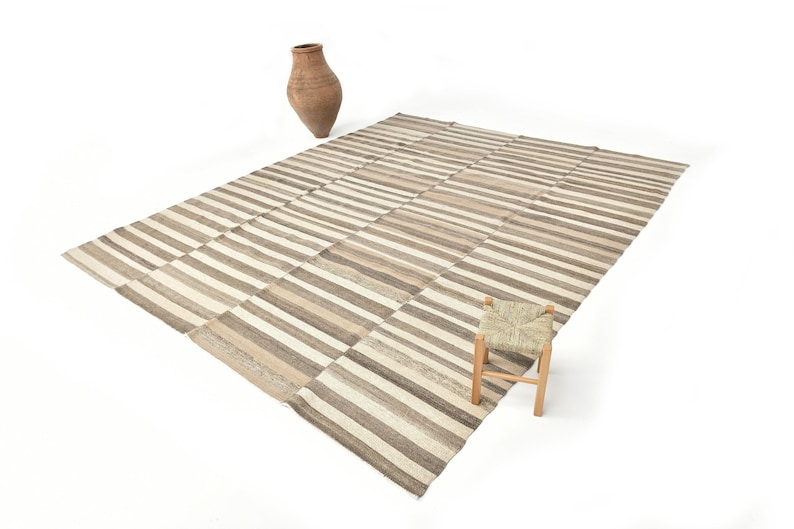 May include: A striped rug with a woven stool in front of it. The rug is made of natural fibres and has a light brown and white colour scheme.
