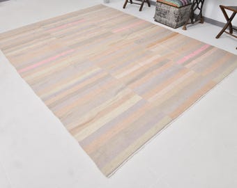 May include: A large rectangular area rug featuring a flat-woven texture with horizontal stripes in muted shades of beige, cream, soft lavender, and pale pink. The design consists of repeating bands of varying widths across the entire surface.