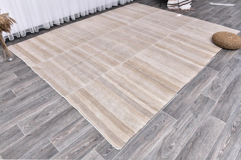 Pu&ograve; includere: Un tappeto beige e bianco a strisce con un leggero bagliore. Il tappeto &egrave; steso su un pavimento in legno.