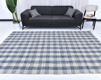 May include: A blue and white checkered rug with a woven texture. The rug is rectangular and covers a large area of the floor. A dark gray sofa with two gray pillows is in the background.