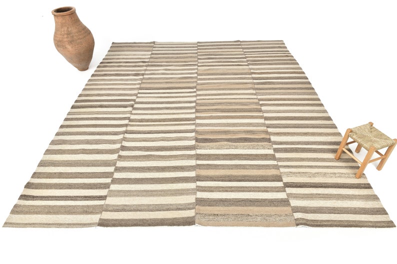 May include: A striped rug with a beige and brown colour scheme. The rug is made of wool and has a hand-woven texture.